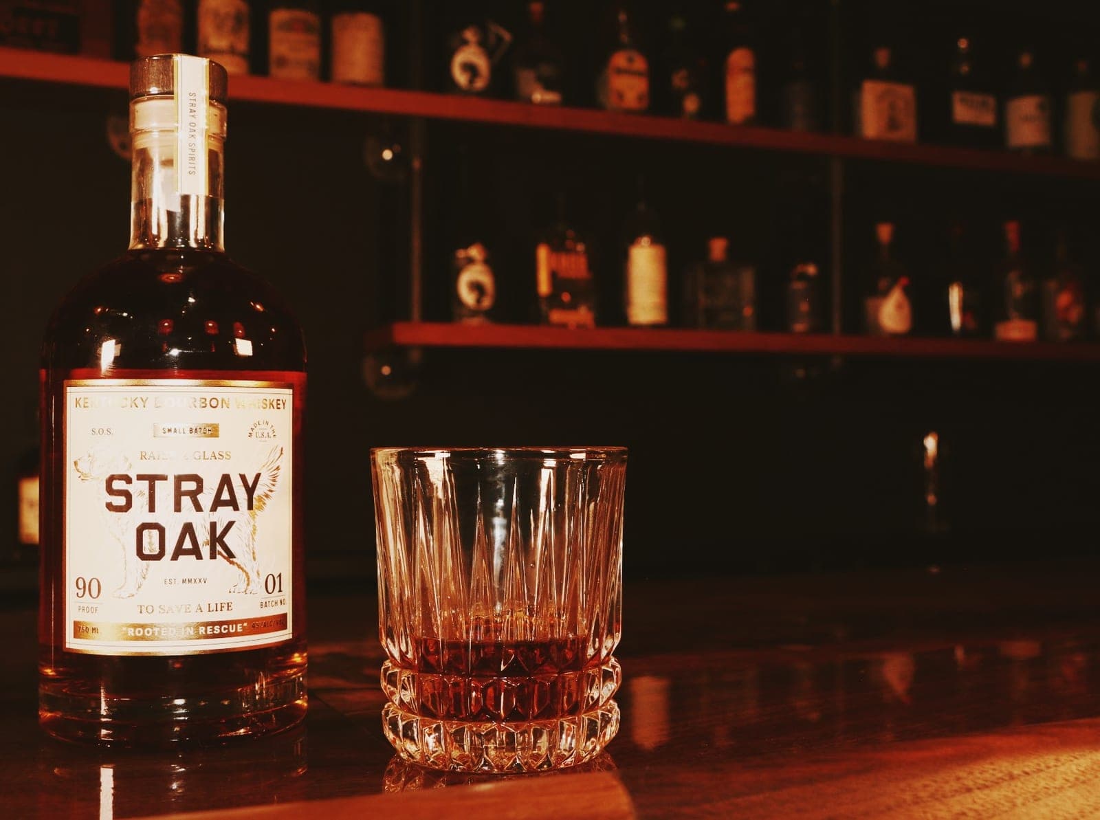 A bottle of Stray Oak bourbon and a glass poured neat on a bar top